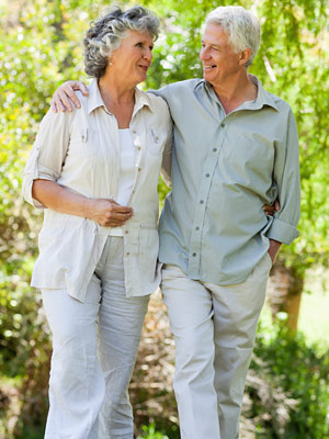 An elderly man and woman taking a walk outside, his arm placed around her